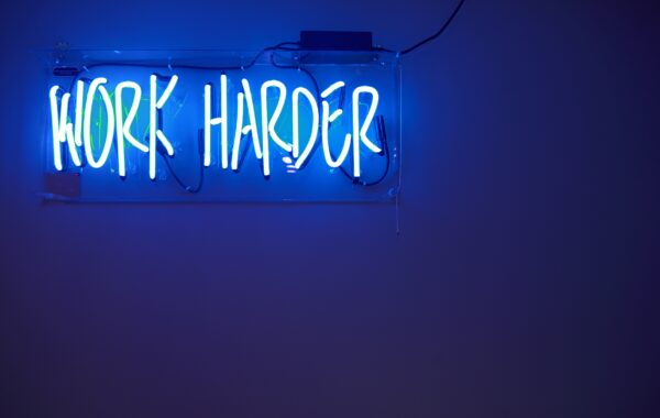 electric blue neon sign saying “work harder”
