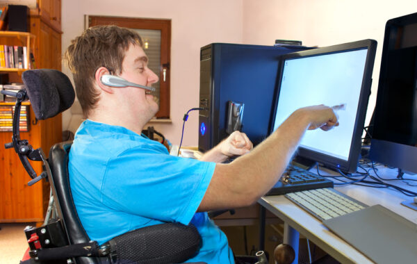 A disabled person using a computer with assistive technology. The person is pointing at or touching the computer screen.